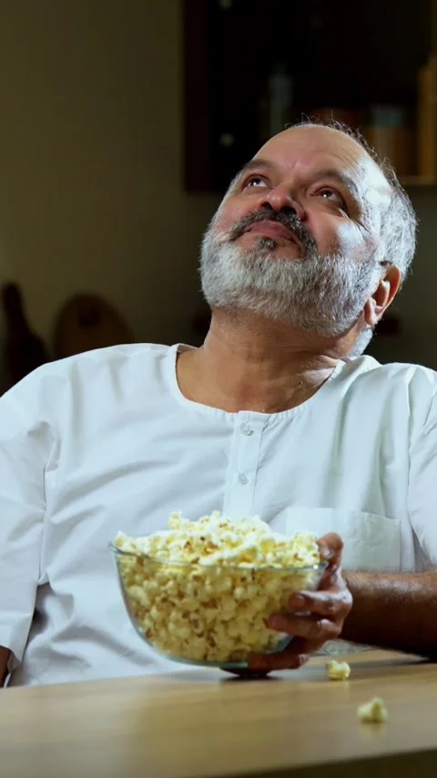 Senior Indian man sitting with snacks, reacting joyfully to tasty Stock Footage 343107037