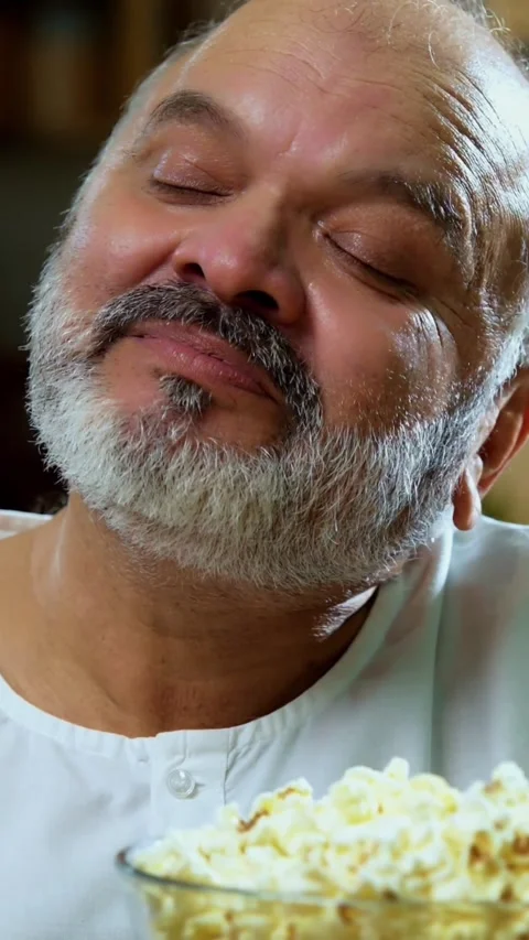Senior Indian man sitting with snacks, reacting joyfully to tasty Stock Footage 343107047