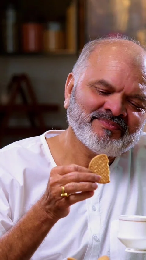 Senior Indian man sitting with snacks, reacting joyfully to tasty Stock Footage 343107235