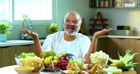 Senior Indian man sitting with snacks, reacting joyfully to tasty Stockbeeldmateriaal 343138879