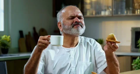 Senior Indian man sitting with snacks, reacting joyfully to tasty Video stock 343139102