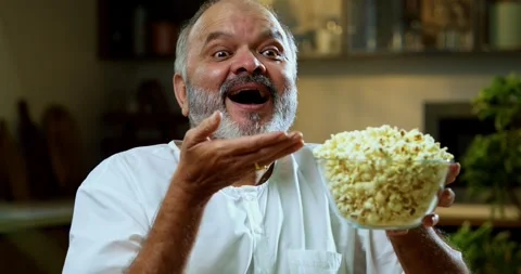 Senior Indian man sitting with snacks, reacting joyfully to tasty Stock Footage 343139521