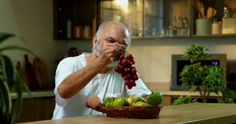 Senior Indian man sitting with snacks, reacting joyfully to tasty 動画素材 343139866