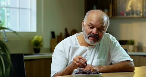 Senior Indian man sitting with snacks, reacting joyfully to tasty Stockbeeldmateriaal 343140001