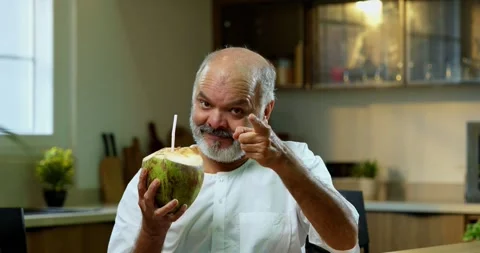 Senior Indian man sitting with snacks, reacting joyfully to tasty Stockbeeldmateriaal 343140107