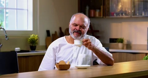 Senior Indian man sitting with snacks, reacting joyfully to tasty 스톡 동영상 343140879