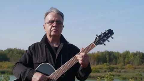 Senior individual creating melodies while gazing across tranquil lake Stock Footage 331664638