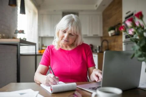 Senior lady at kitchen table taking notes using notebook Stock Photos