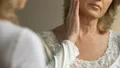 Senior lady looking in mirror at her skin, waiting for effect of anti-age cream HD Footage