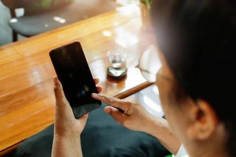 Senior lady smiling cheerfully while sitting in a chair and reading the lates Stock Photos