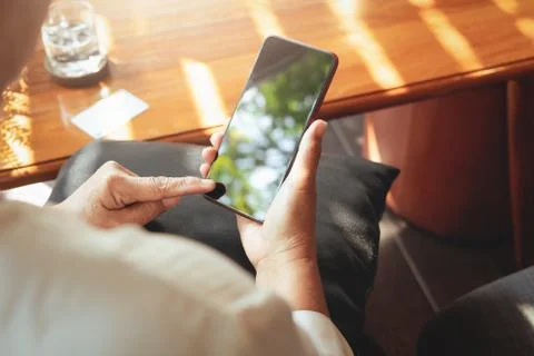 Senior lady smiling cheerfully while sitting in a chair and reading the lates Stock Photos