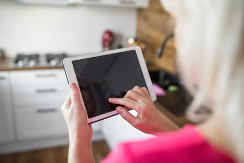 Senior lady standing at kitchen using tablet Stock Photos