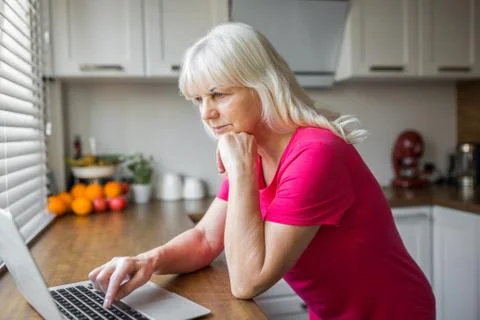 Senior lady using laptop on kitchen counter Foto stock