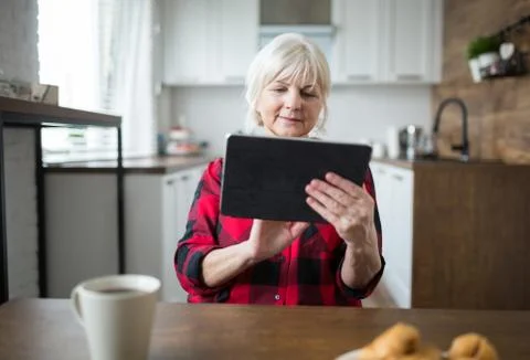 Senior lady using tablet at kitchen table Stock Photos