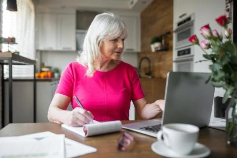Senior lady working at kitchen table using notebook Stock Photos