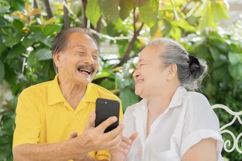 Senior lover enjoying while doing video call via app on phone. Older Asian .. Stock Photos