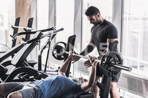 Senior male doing exercises with his trainer in athletic center Stock Photos