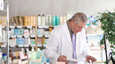 Senior male pharmacist uses computer at workplace. Girl colleague in background Stock Footage 326311389