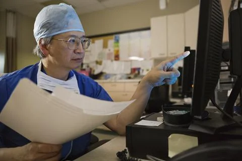 Senior male surgeon using computer to review medical records in clinic Foto stock