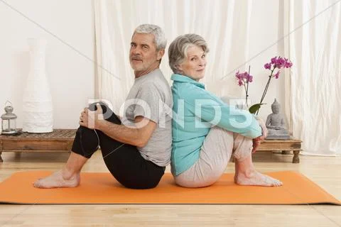A senior man and a senior woman sitting back to back on an exercise mat Stock Photos