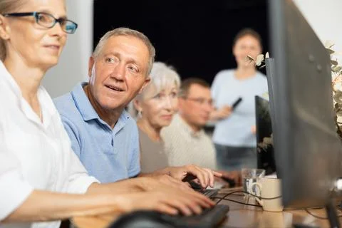 Senior man attending computer class under guidance of female teacher Stock Photos