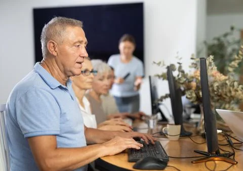 Senior man attending computer class under guidance of female teacher Fotos de archivo