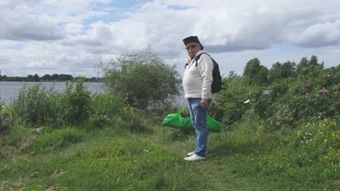 Senior man with backpack and bag walks along riverbank Stock Footage 139796444