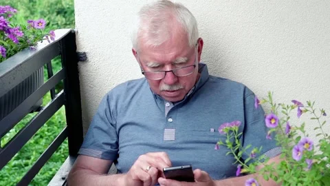 Senior man browsing smarthone on the balcony Видео 114428226