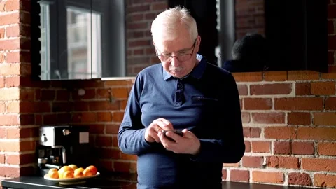Senior man browsing smarthone in the kitchen Видео 87625733