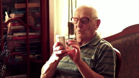 Senior man browsing smarthone by table at home, slow motion Stock Footage 105353296