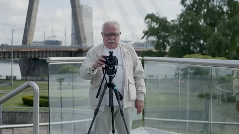 Senior man with camera on tripod talks on city street Stock Footage 136753506