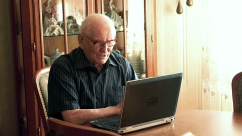 Senior man chatting on laptop by table at home Видео 100158027
