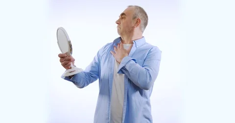 Senior man checking his face in the mirror. Isolated on white. Stock Footage 128838996