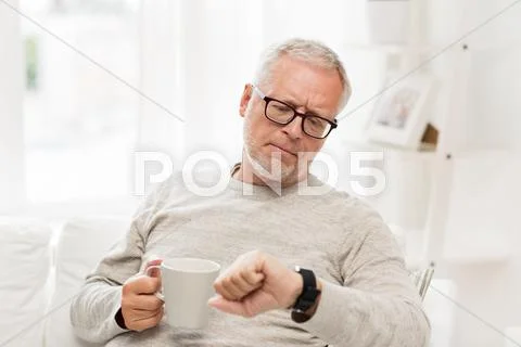 Senior man with coffee looking at wristwatch Stock Photos