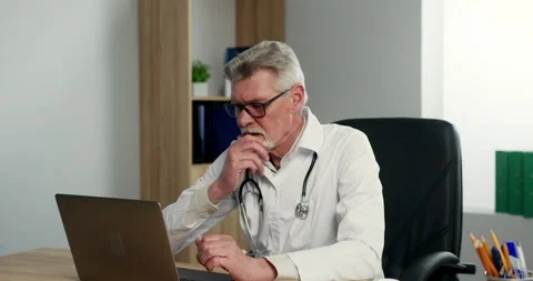 Senior man doctor working on computer in hospital office, looking serious and 库存影片 155647618