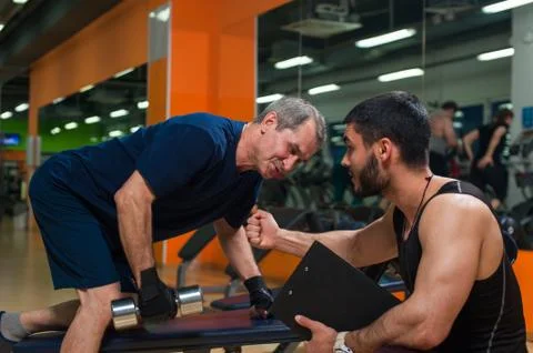 Senior man doing weight exercise with trainer. Stock Photos