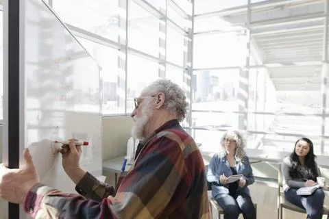 Senior man drawing support network diagram on whiteboard in meeting Stock Photos