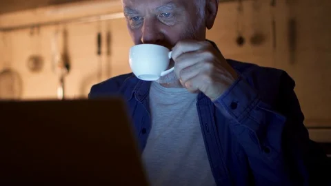 Senior man drinking coffee from cup while using laptop. Freelancer at night Stock Footage 94344318