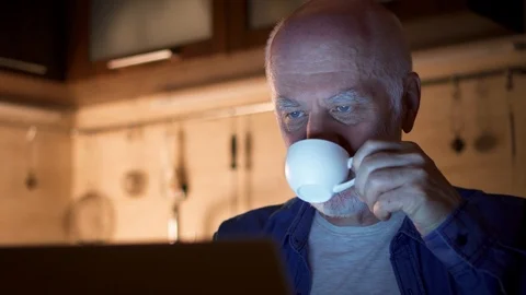 Senior man drinking coffee from cup while using laptop. Freelancer at night Stock Footage 95808152