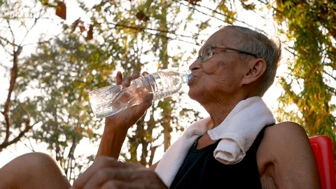 Senior man drinking water from bottle while exercise in a park on sunshine day. Video stock 129231201