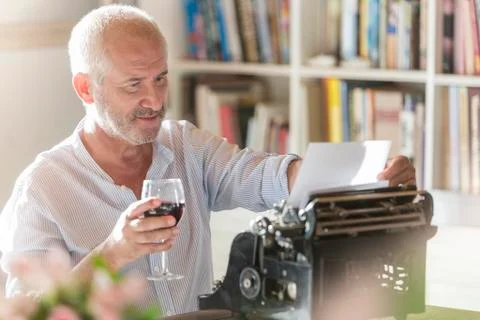 Senior man drinking wine at typewriter in study Stock Photos