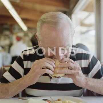 A Senior Man Eating A Hamburger