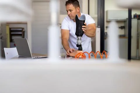 Senior man examining prosthetic socket and pylon in laboratory, with laptop and Stock Photos