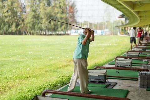 Senior man exercise practicing his golf swing at golf driving range. Stock Photos