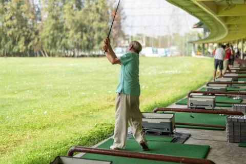Senior man exercise practicing his golf swing at golf driving range. Stock Photos