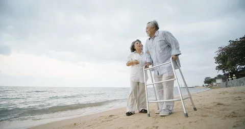 Senior man exercise with walker and his wife assist him walking along beach. Stock Footage 102860278