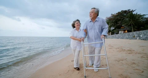 Senior man exercise with walker and his wife assist him in beach. Video stock 102875760