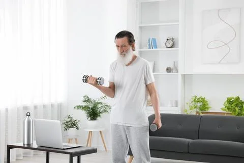 Senior man exercising with dumbbells while watching online tutorial at home.. Foto stock