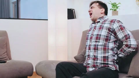 Senior man experiencing back pain while reaching for the remote on a couch in a Stock Footage 301581617