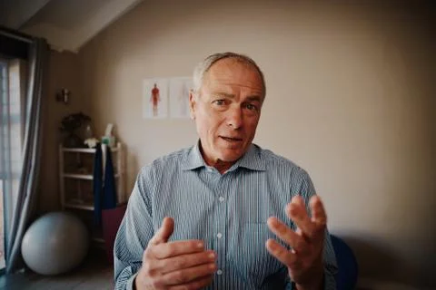 Senior man explaining with hand gesture looking at camera in physiotherapy room Stock Photos